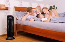 Čistička vzduchu Ionic-CARE v ložnici vedle postele ve které si povídají matka, otec a jejich 2 malé děti, barva černá