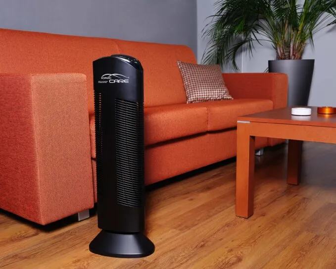 Čistička vzduchu Ionic-CARE v celkovém pohledu v obývacím pokoji s oranžovou pohovkou, barva černá
