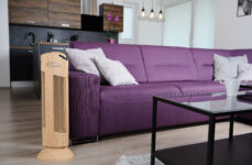 Čistička vzduchu Ionic-CARE v interiéru s fialovou pohovkou, dekor dřevo dub