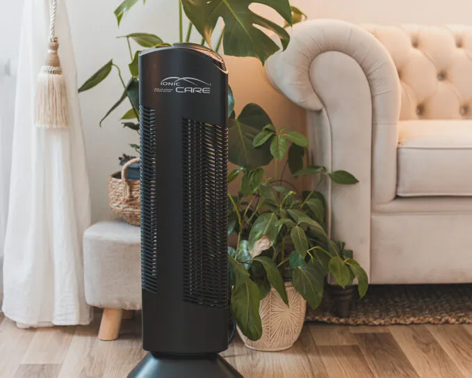 Čistička vzduchu Ionic-CARE v interiéru se světlou pohovkou, dlouhou záclonou a pokojovou rostlinou monsterou, barva černá