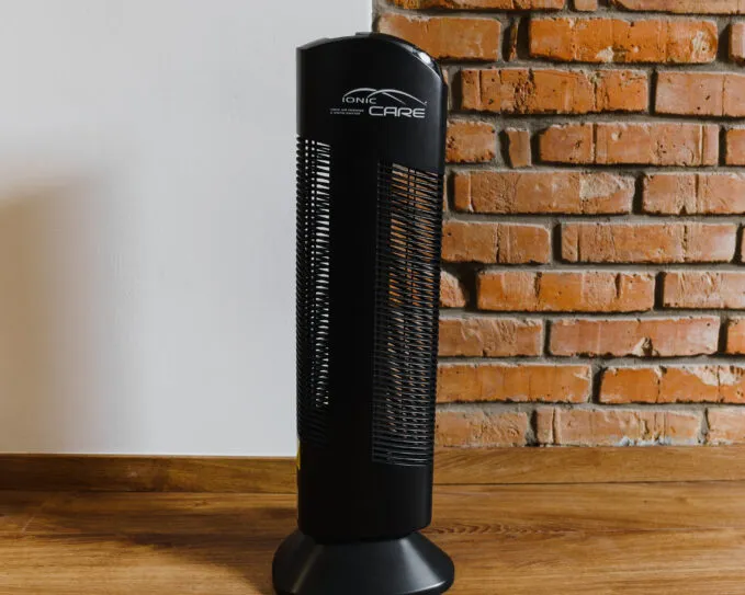 Čistička vzduchu Ionic-CARE v interiéru před bílou a cihlovou zdí , barva černá