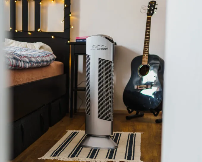 Čistička vzduchu Ionic-CARE v ložnici s černou postelí a kytarou opřenou o zeď, barva stříbrná