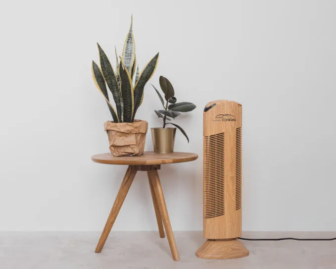 Čistička vzduchu Ionic-CARE v interiéru s odkládacím stolkem a rostlinami v květináči, dekor dřevo dub