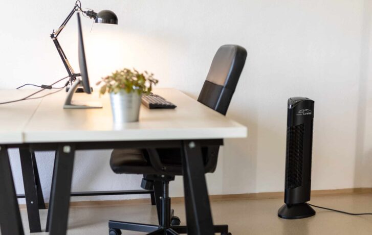 Kancelářský pracovní stůl se žídlí a lampou, vedle kterého stojí čistička vzduchu Ionic-CARE v černé barvě